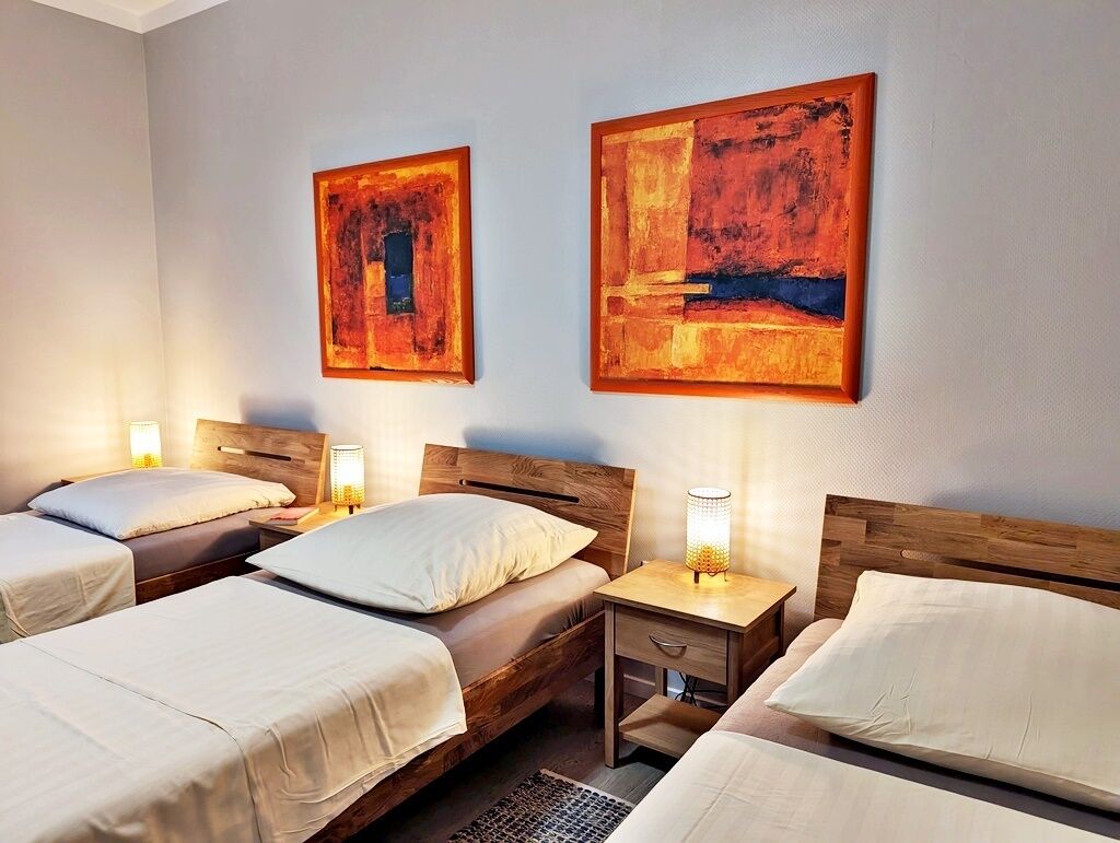 A hotel room with two single beds, each with a wooden headboard, a bedside table with a lamp, and artwork on the wall.
