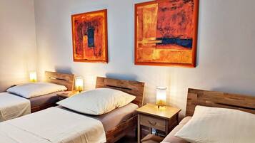 A hotel room with two single beds, each with a wooden headboard, a bedside table with a lamp, and artwork on the wall.