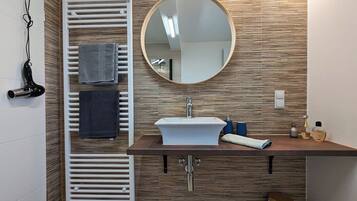 A modern bathroom with a built-in sink, a round mirror, a towel rack, and a hairdryer.
