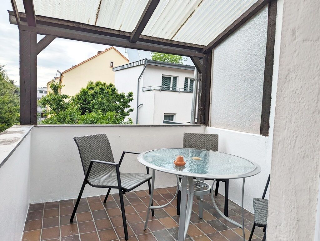 A covered balcony with a round glass table and four chairs.