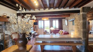 A rustic interior with exposed wooden beams, a stone wall, a dining table with benches, a sofa, and a vase with white flowers. - La Chalaumière (Chalaux)