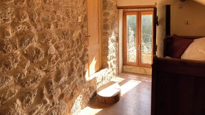 A rustic room with stone walls, a wooden door, and a bed with a wooden headboard. - La Chalaumière (Chalaux)