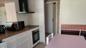 A compact kitchen with white cabinets, a built-in oven, and a microwave. There's a pink table with white chairs and a brown bench in the dining area.