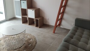 A living room with a flat-screen TV mounted on the wall, a grey sofa, a wooden ladder, and a small wooden cabinet.