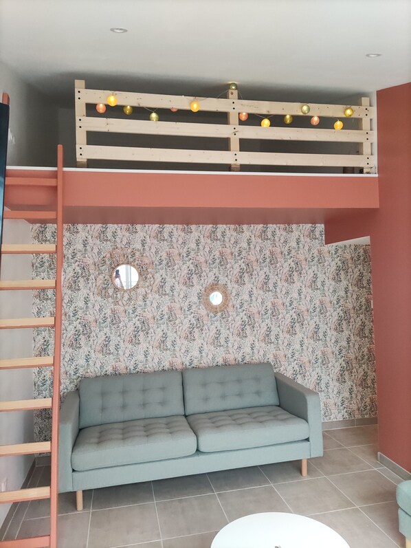 A room with a bunk bed, a sofa, a ladder, and a wall with floral wallpaper. - Maison Avec Jacuzzi, Proche Plages (Avrillé)