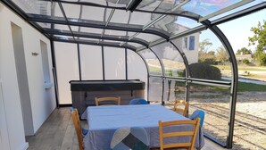 A covered patio with a table and chairs, a grill, and a view of the outdoors.