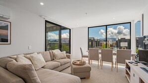 A modern living room with a sofa, dining area, and large windows offering a mountain view. - Winton Wonder - Wanaka Holiday Apartment (Wanaka)