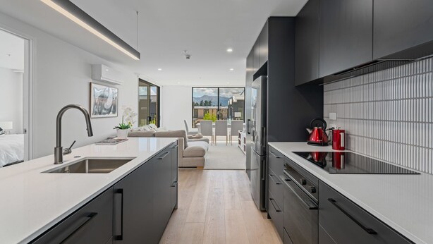 A modern kitchen with a central island, dark cabinetry, and a view of the outdoors. - Winton Wonder - Wanaka Holiday Apartment (Wanaka)