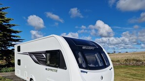 Un camper bianco con la scritta 'SWIFT' e 'SPRITE', parcheggiato in un prato con cielo sereno.