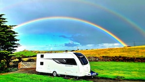 Un camper bianco parcheggiato in un prato erboso, con un arcobaleno sullo sfondo.