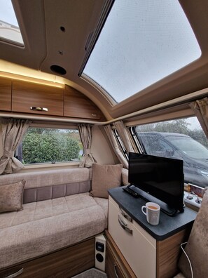 A cozy interior with a cushioned seating area, a flat-screen TV, a coffee mug, and a power outlet. - Brand new Touring Caravan Sited all Setup Ready (Holyhead)