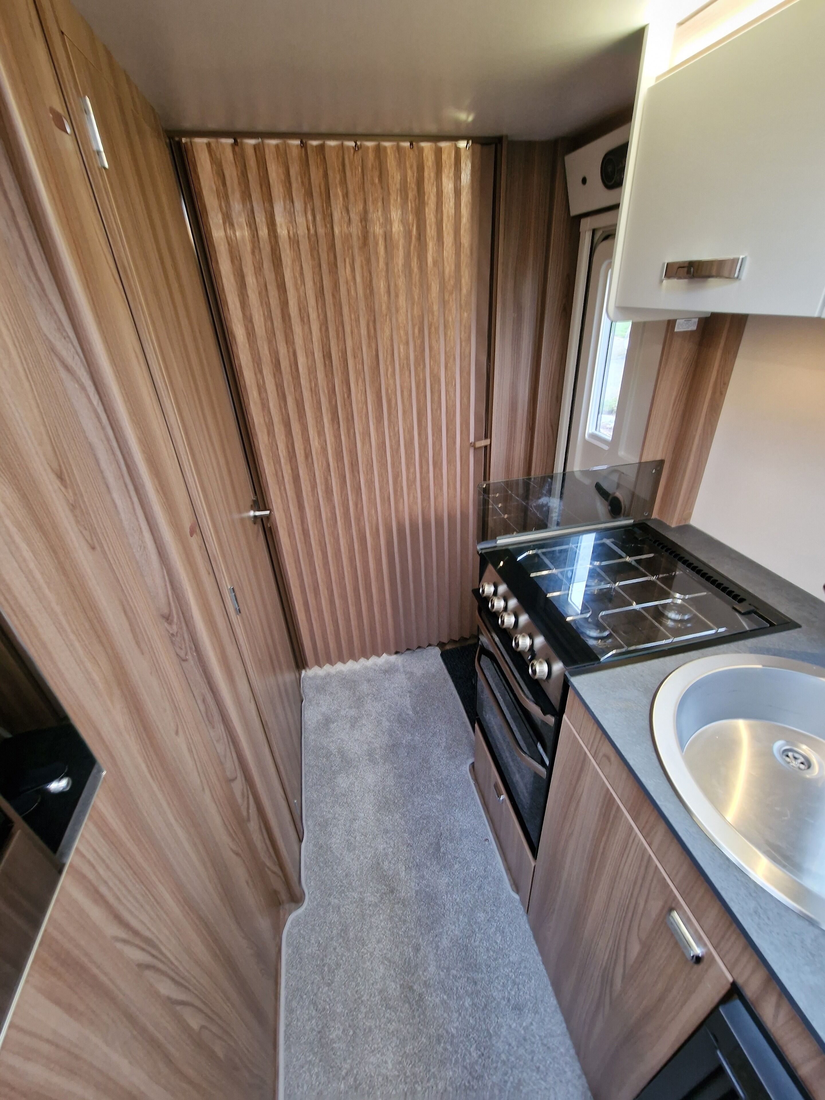 Une cuisine de taille réduite, dotée de meubles en bois, d’un évier en acier inoxydable et d’une cuisinière à gaz.
