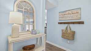 A room with a light blue wall, a white console table with a lamp, a bowl, and a painting of flamingos. - Almost Heaven - Beautiful Oceanfront Condo with a Pool! (Murrells Inlet)