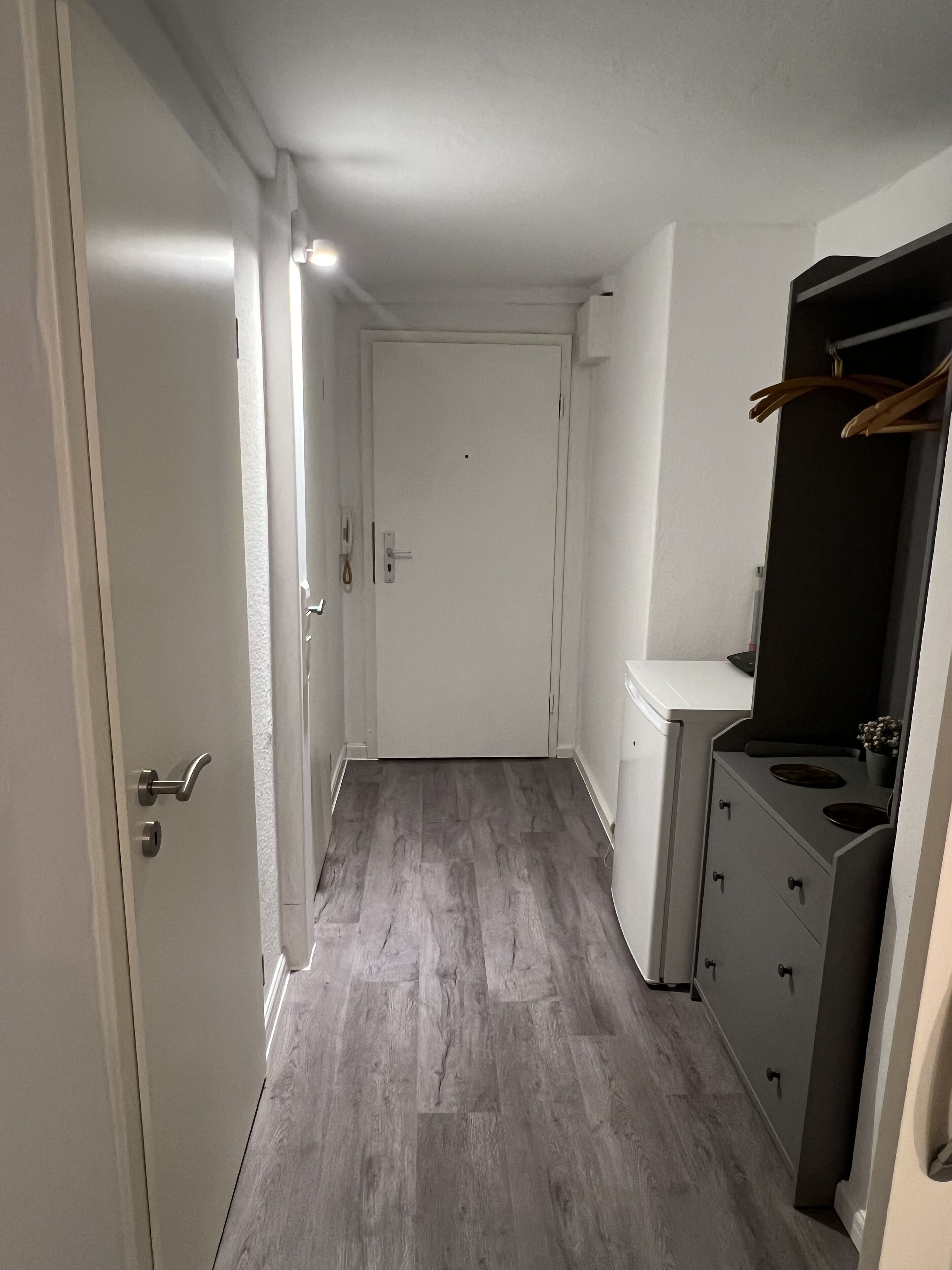 A narrow hallway with a wooden floor, a white door at the end, and a kitchenette area with a stove and cabinets.