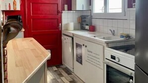 Ett kompakt kök med röda skåp, en träbänkskiva, en diskmaskin, en spis och ett kylskåp.