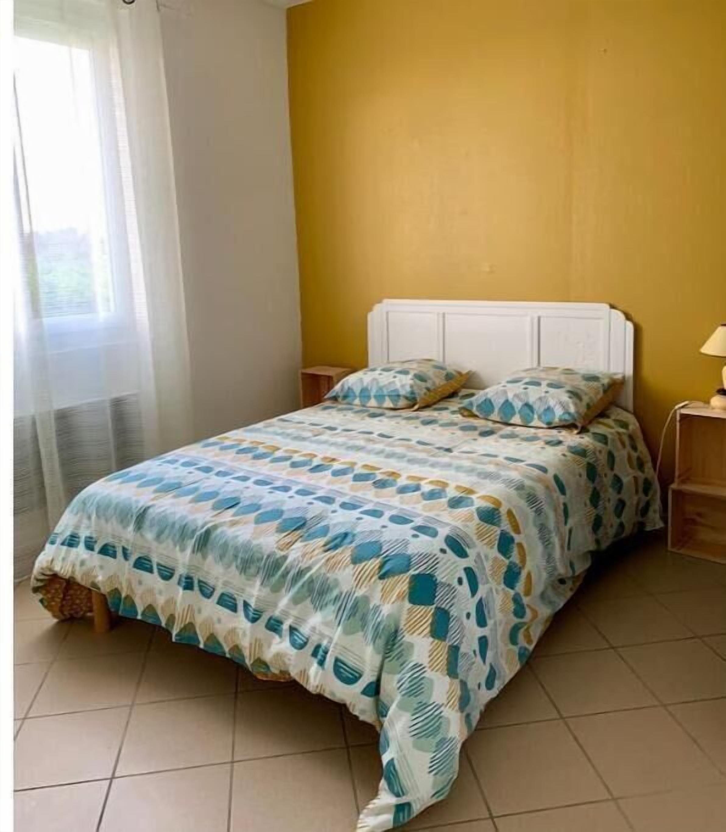 Uma cama com colcha estampada, cabeceira branca e mesa de cabeceira com abajur.