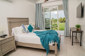 Une chambre à coucher comprenant un lit, une table de chevet, une commode, une chaise, un téléviseur et une vue sur l’extérieur.