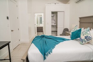 Une chambre à coucher avec un lit, un bureau et une chaise. On peut voir une armoire et une salle de bain à travers une porte ouverte.