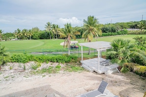 Un parcours de golf agrémenté d’un pavillon, de palmiers et d’un ciel dégagé.