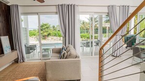 Sala de estar moderna com sofá, mesa de centro e vista para uma piscina e área externa com assentos.