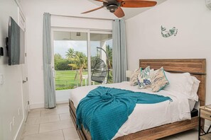 A bedroom with a bed, a ceiling fan, a TV, and a view of a garden through a sliding door.