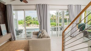 Un'ampia zona giorno con divano, tavolo da pranzo e vista su piscina e area salotto esterna.