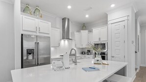 A modern kitchen with white cabinetry, stainless steel appliances, and a central island with seating. - Prominence Townhome with LSV and Bikes (Watersound)