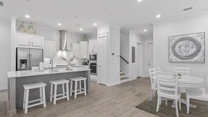 A modern kitchen with white cabinetry, a central island with stools, a dining area with a table and chairs, and a staircase leading to another level. - Prominence Townhome with LSV and Bikes (Watersound)