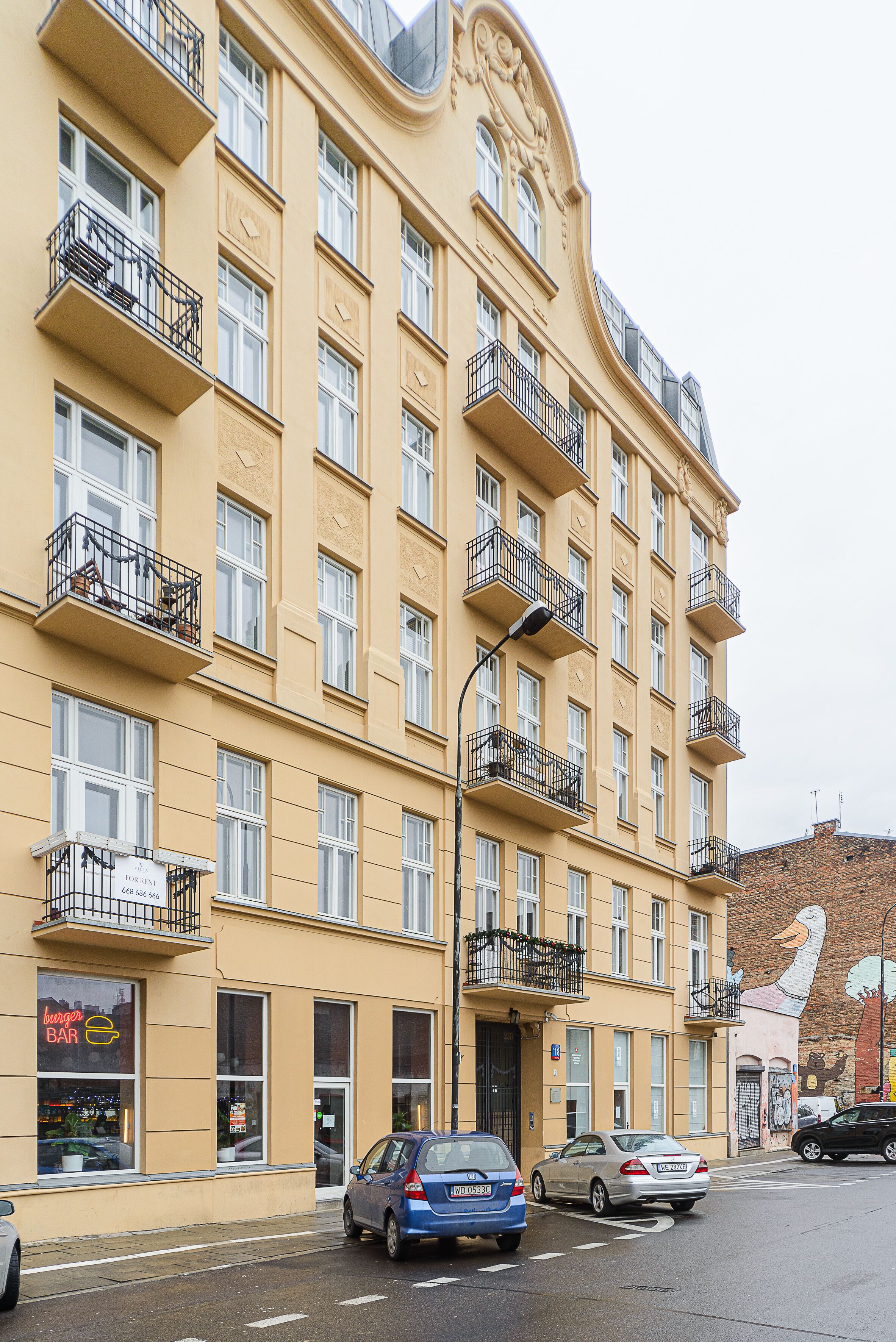 Ein mehrstöckiges Gebäude mit Balkonen, ein Restaurant im Erdgeschoss und ein Wandgemälde an der Seite.