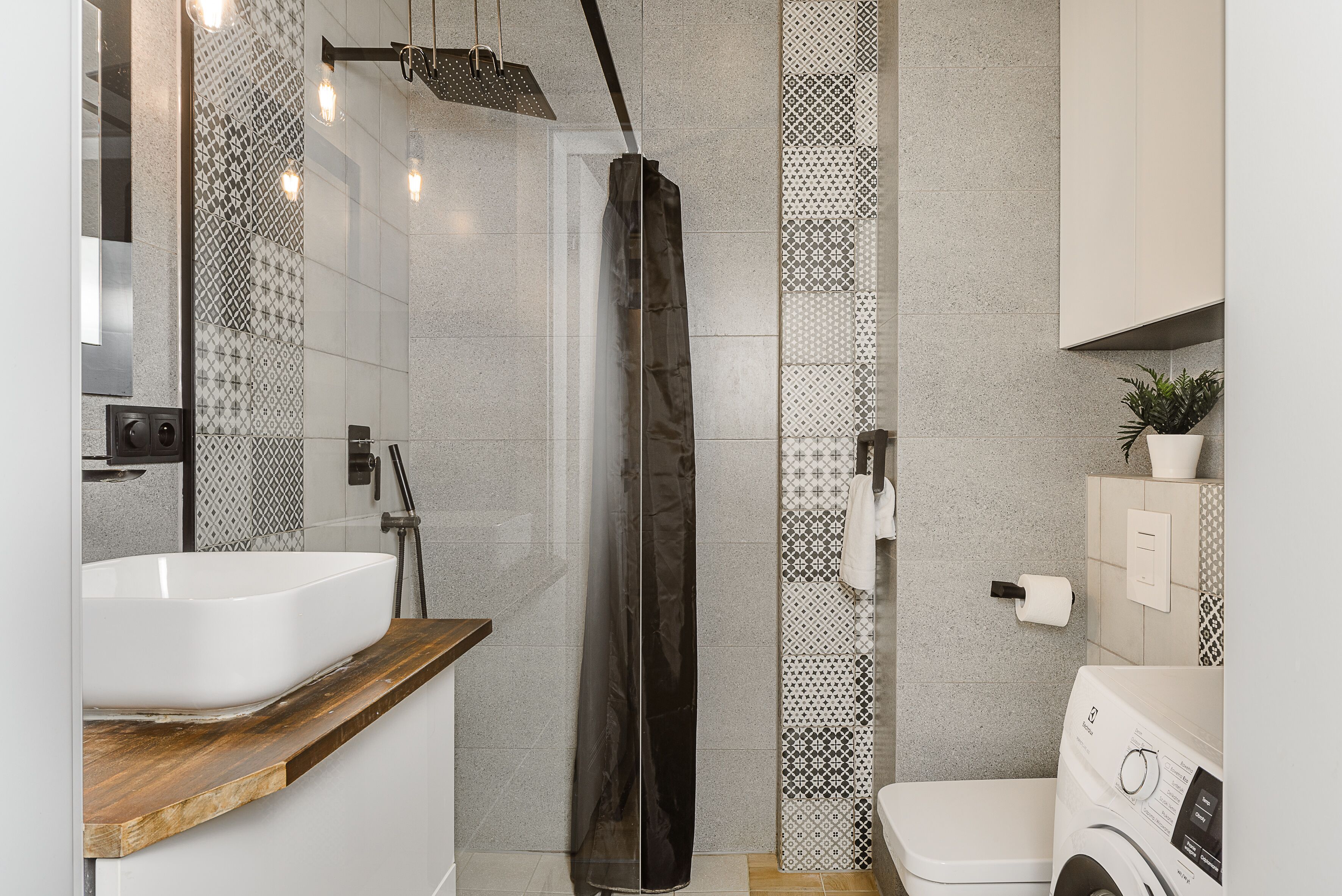 A modern bathroom with a large white sink, a shower with a black curtain, and a washing machine.