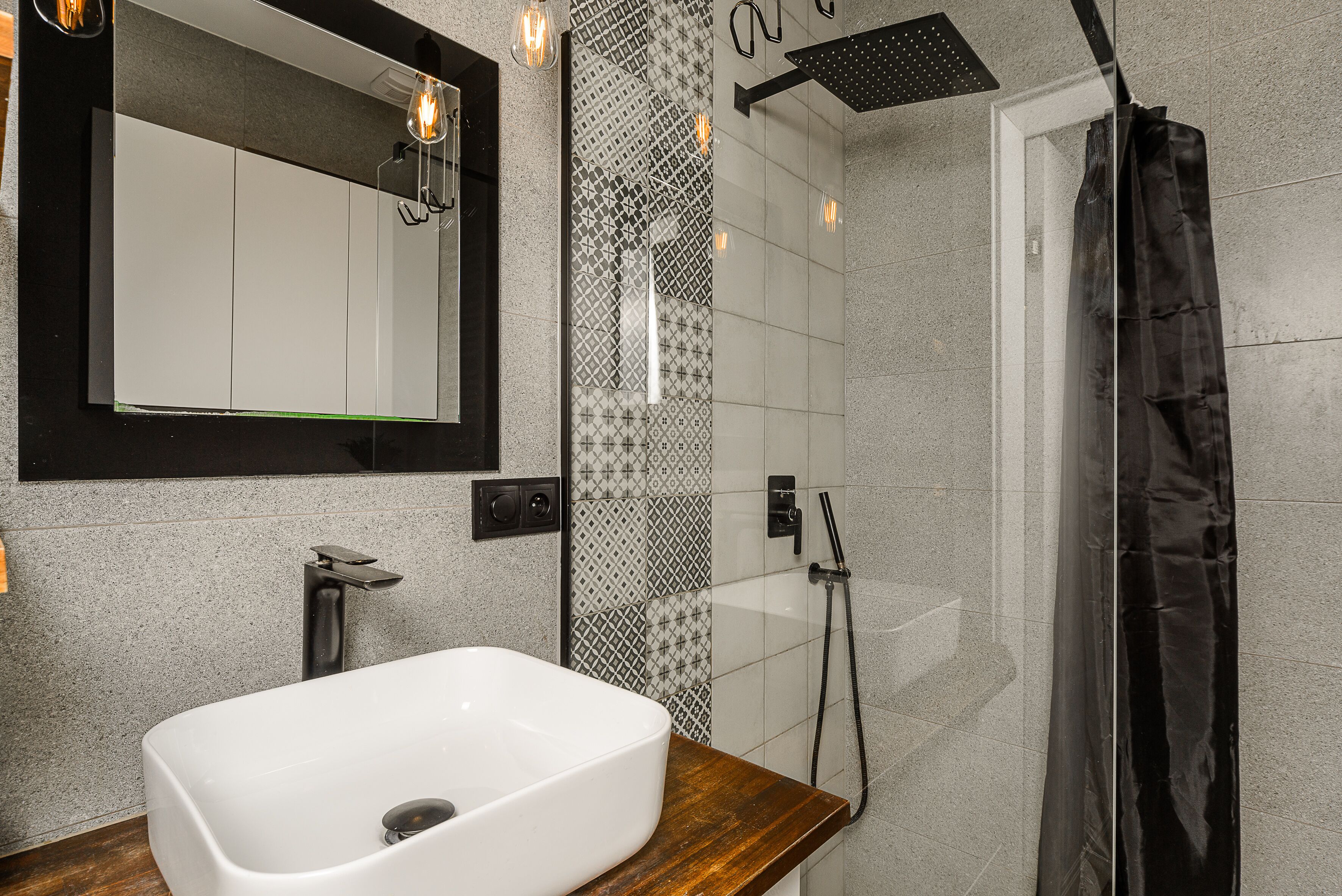Une salle de bain moderne avec un lavabo rectangulaire, un miroir, une douche et un mur décoré d’un motif.