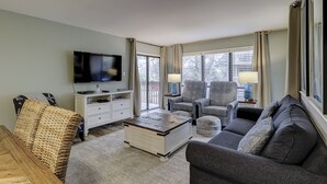 A modern living room with a flat-screen TV, two armchairs, a sofa, a coffee table, and a TV stand.