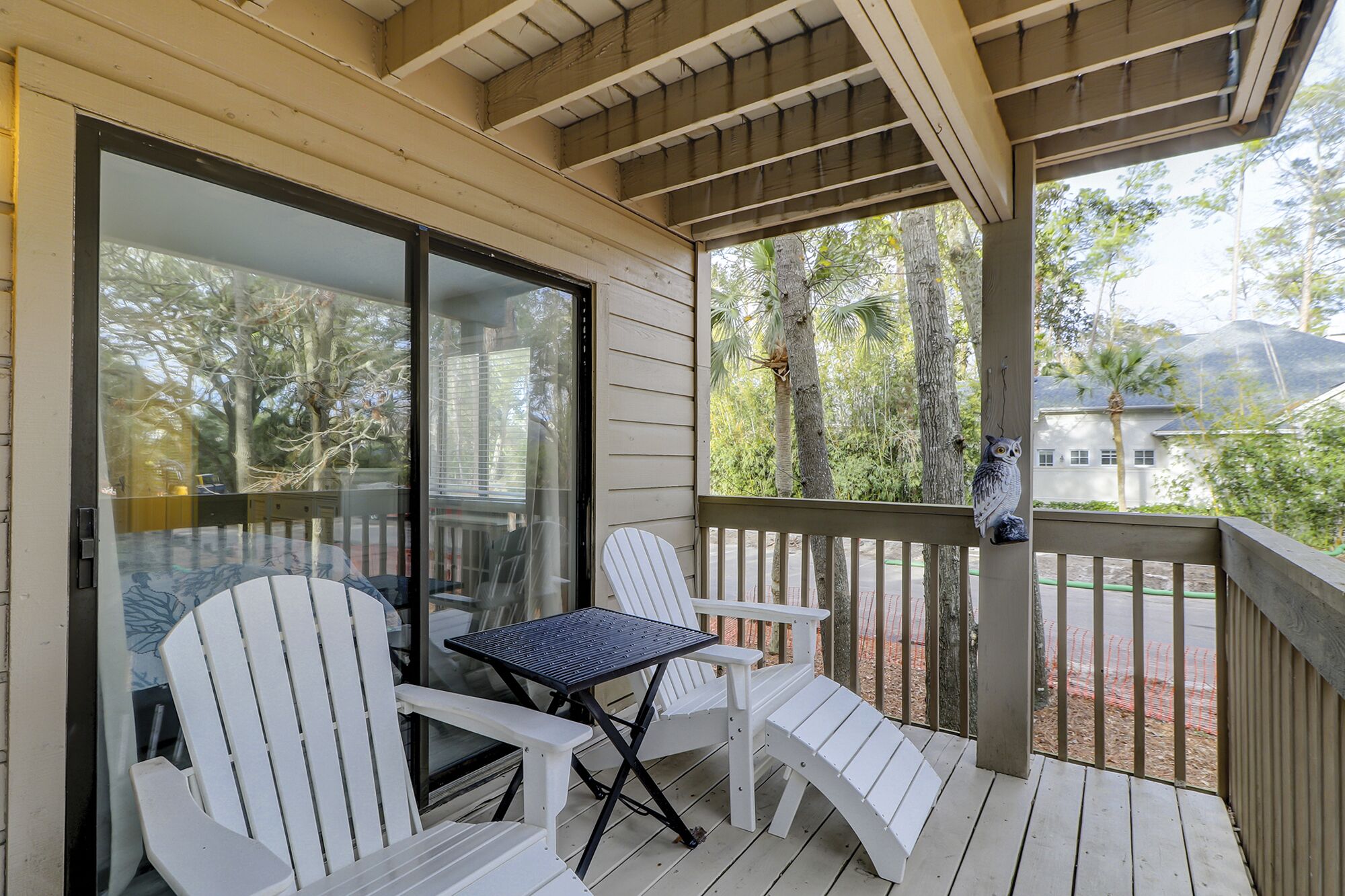 A covered porch with white Adirondack chairs and a small table, overlooking a residential area with trees and houses.