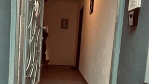 Um corredor com portão de metal, piso cerâmico e interfone fixado na parede.