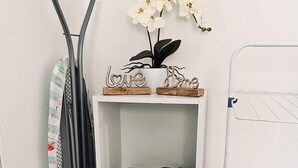Uma prateleira branca com uma orquídea em vaso, um secador de cabelo preto e uma caixa de produtos para cabelo.