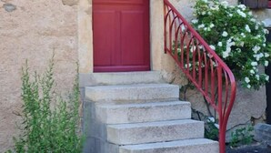 Une porte rouge avec une petite fenêtre, un escalier en pierre et une main courante en métal.