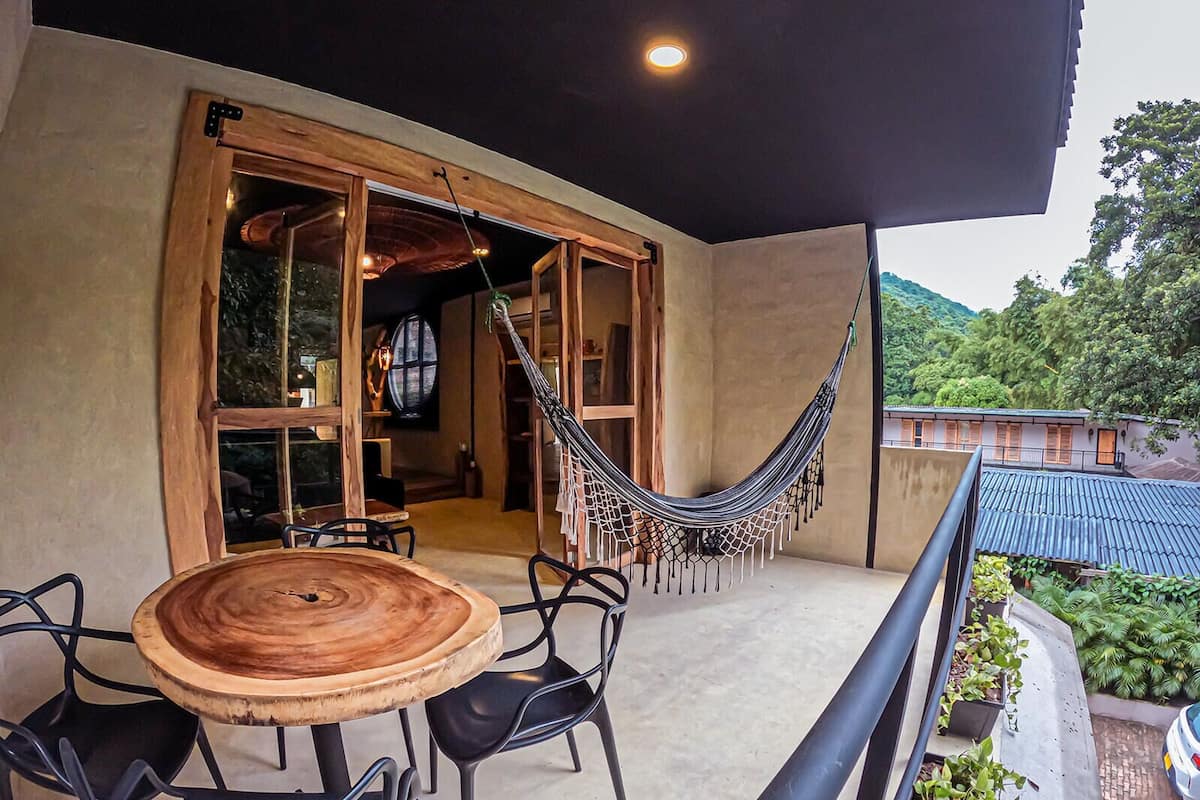 A balcony with a hammock, a round wooden table, and black chairs.