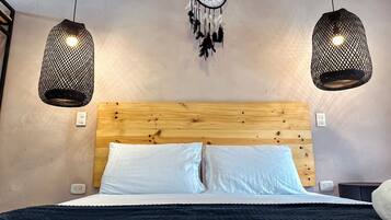 Un dormitorio con cabecera de madera, dos lámparas colgantes y un atrapasueños.