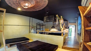 Un interior moderno con sofá, banca, escalera de madera y zona de cocina con luces colgantes.