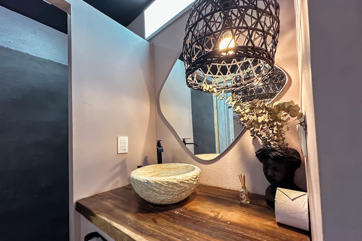 A bathroom with a wooden vanity, a round sink, a mirror, a decorative light fixture, and a wall-mounted faucet.
