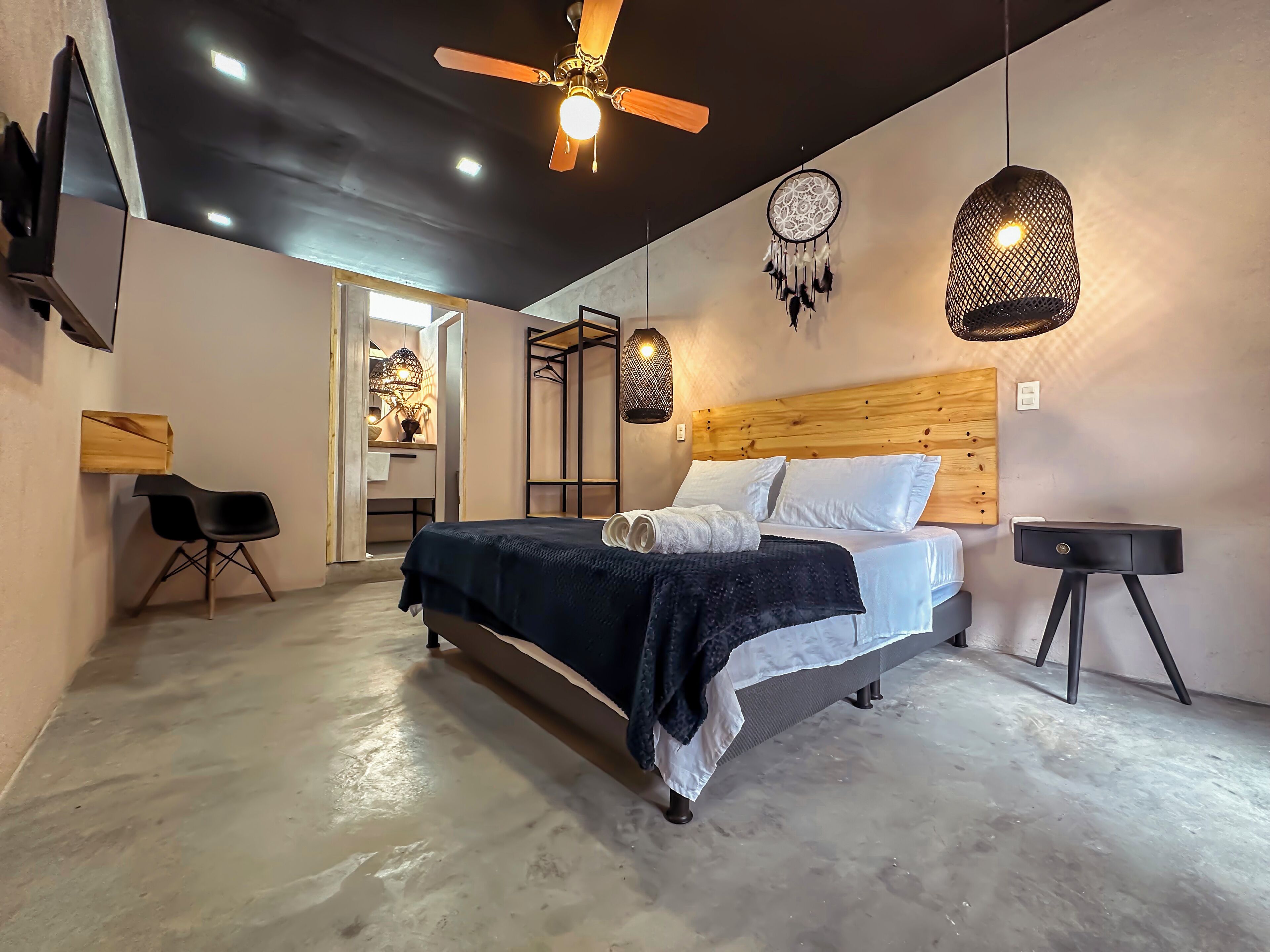 A modern bedroom with a bed, a ceiling fan, a dreamcatcher, and a hanging light fixture.