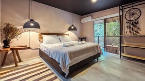 Un dormitorio moderno con una cama grande, dos lámparas de noche, un atrapasueños y vistas a zonas verdes por la ventana.