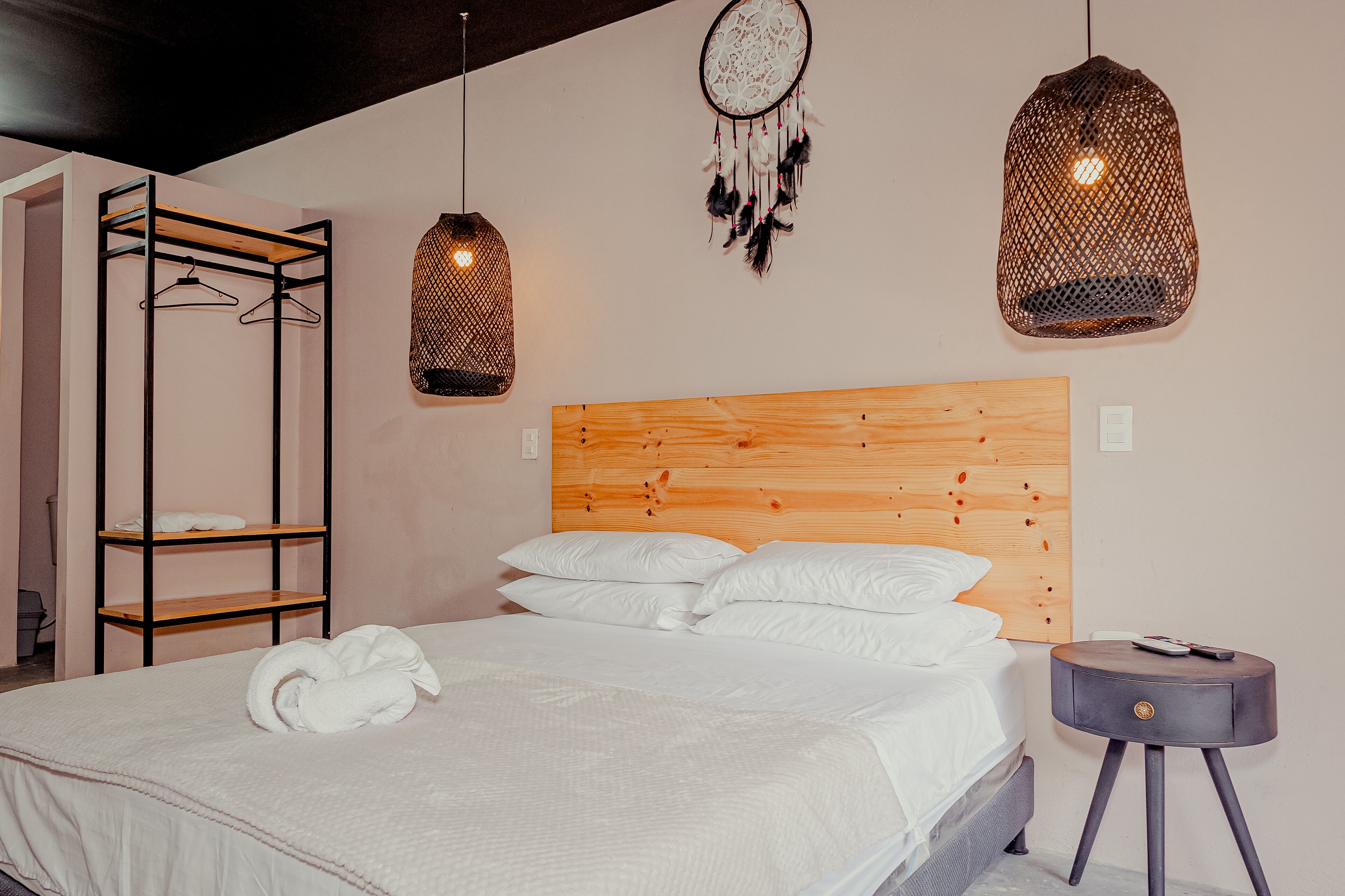 Una cama bien hecha con sábanas blancas, cabecera de madera y mesita de noche con un control remoto.
