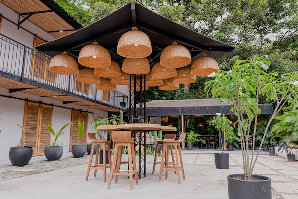 An outdoor dining area with a wooden table and chairs, surrounded by potted plants and a large umbrella. - Hotel Casa de Hadas (Santa Marta)