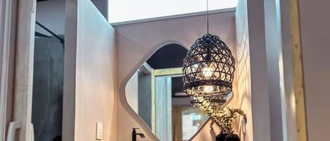 A bathroom with a round mirror, a sink with a woven basin, a towel rack, and a decorative light fixture.