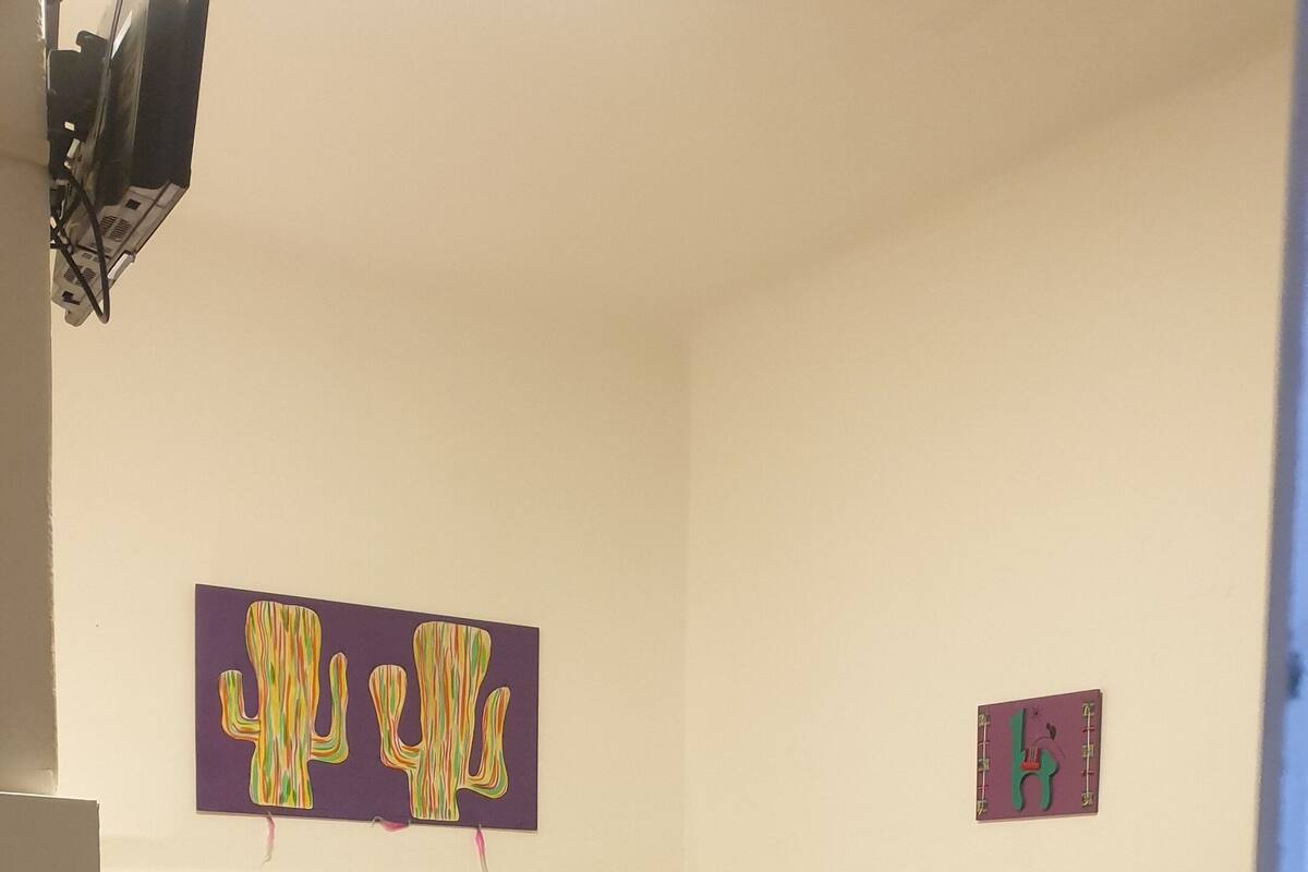 A bedroom with a bed, a headboard, a wall-mounted TV, and two wall art pieces.