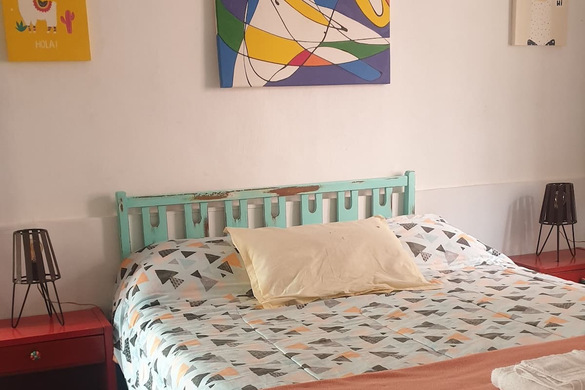 A bedroom with a bed, a nightstand, a lamp, and a wall with artwork.
