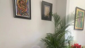 Et spiseområde med et hvidt bord og stole, en stor potteplante og billeder på væggen.