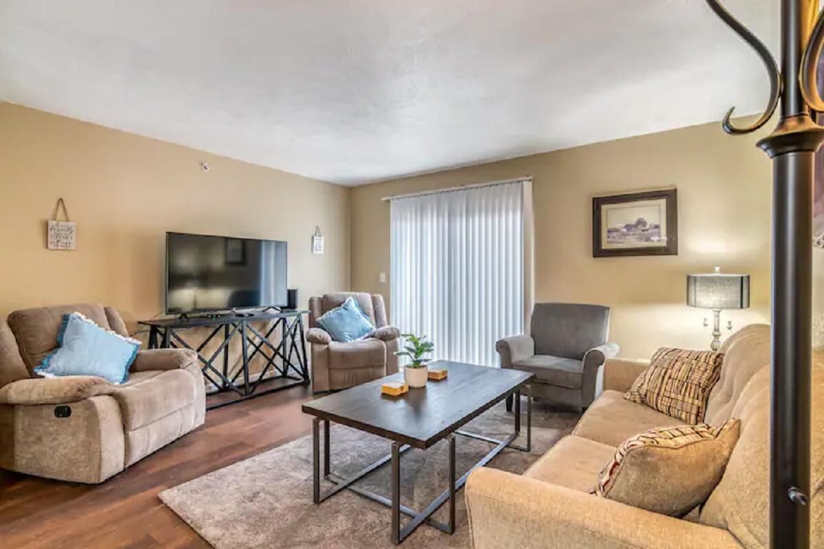 A living room with a sofa, armchairs, a coffee table, a TV, and a window with curtains.