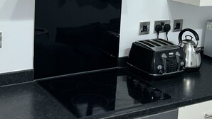 Una cocina con encimera negra, campana extractora de acero inoxidable, tostadora y hervidor.